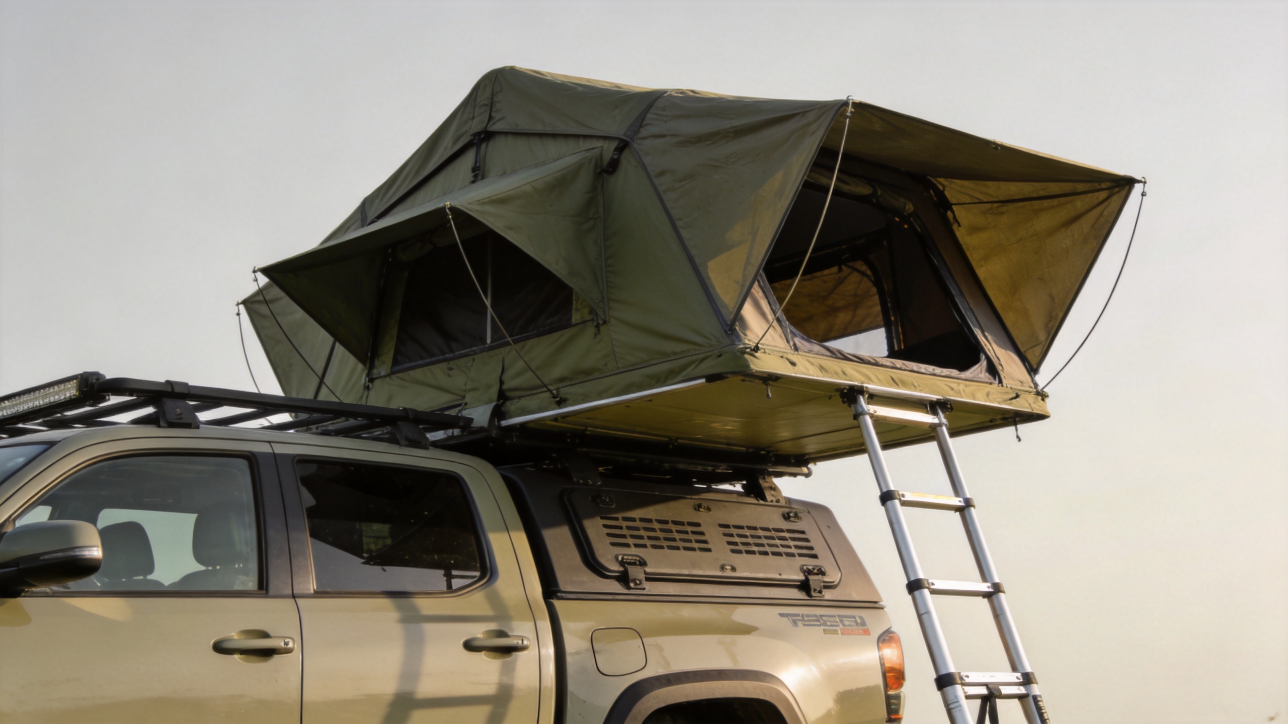 Hardshell roof top tent fully deployed on a vehicle at a campsite with ladder extended