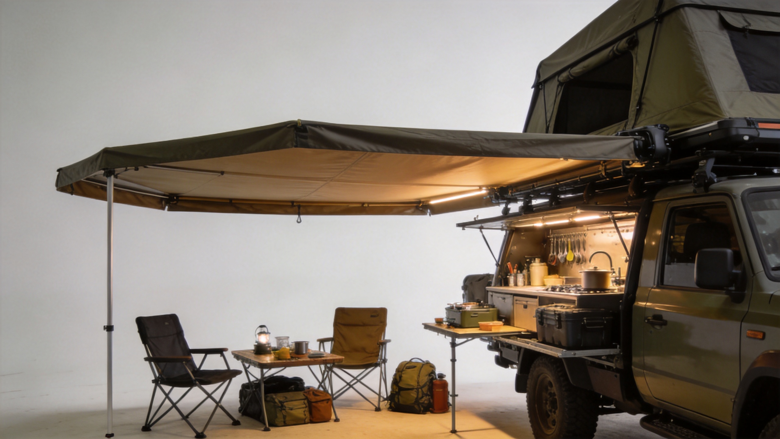Outdoor campsite living space set up under a vehicle awning with camp kitchen and seating area